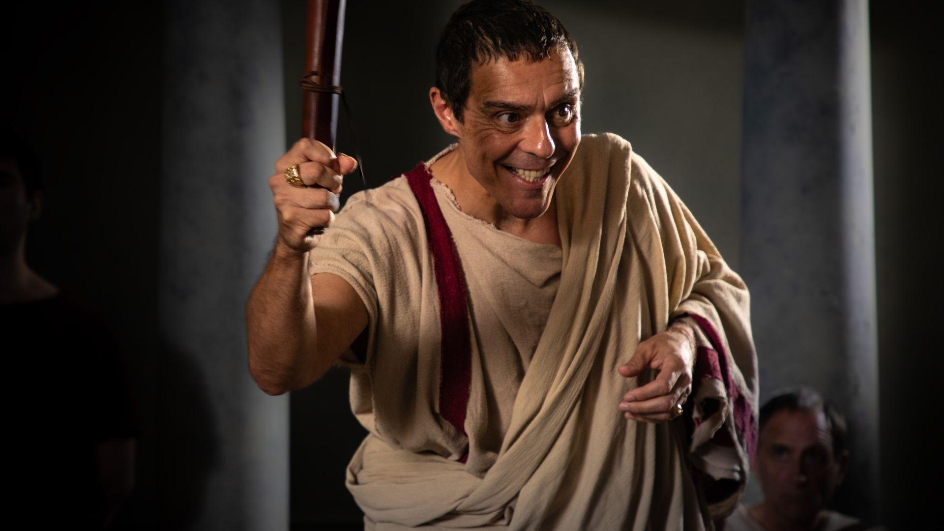 Caesar (played by Andonis Anthony) holds a scroll